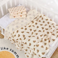 Cream printed cotton muslin swaddle blanket folded on a cot mattress
