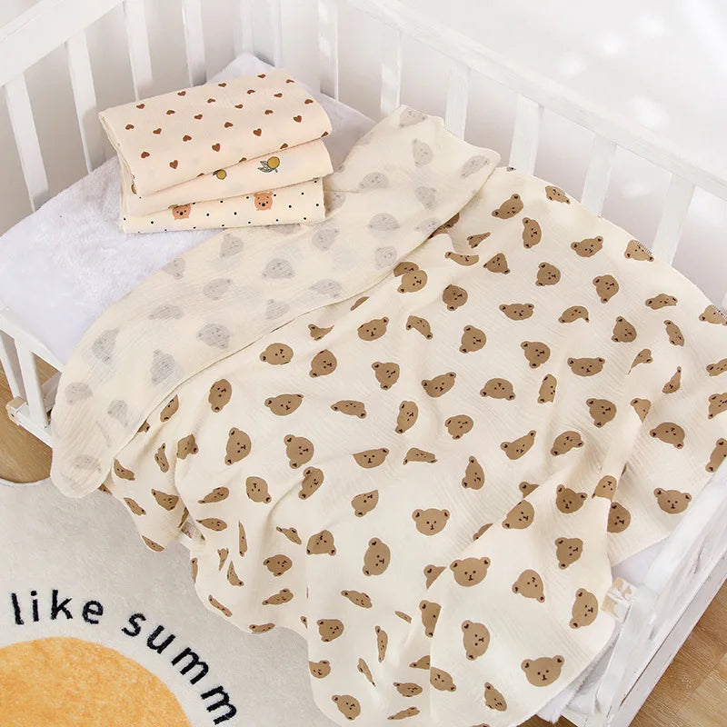 Cream printed cotton muslin swaddle blanket folded on a cot mattress