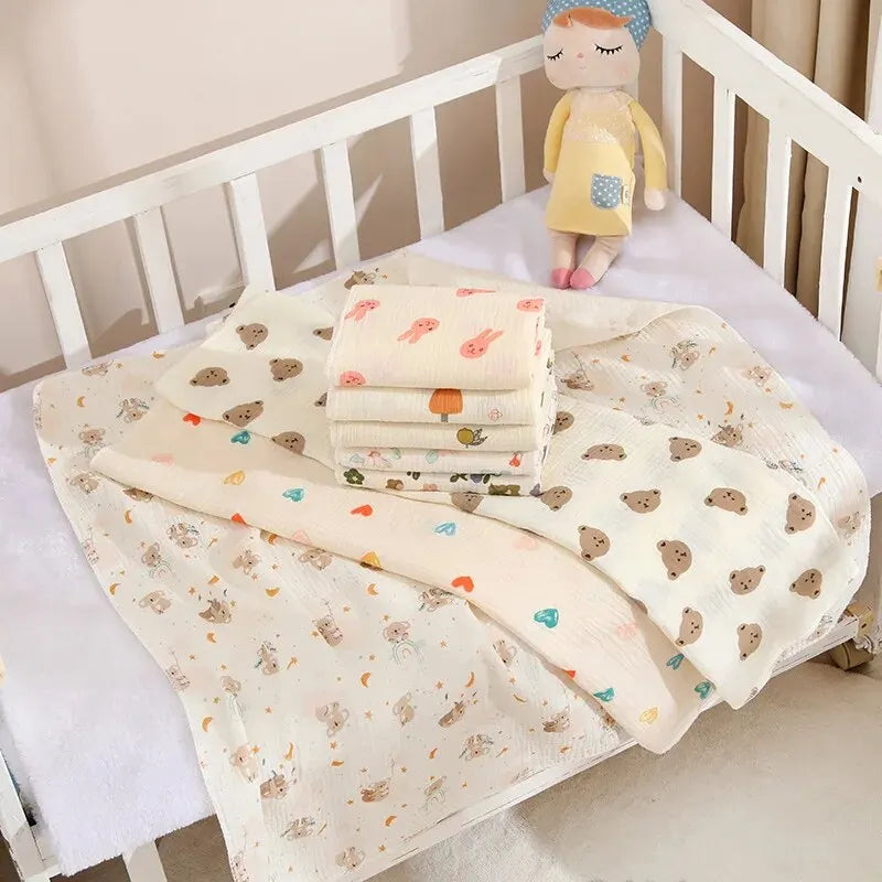 Cream cotton muslin receiving blanket with small bear print, folded in a cot